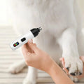 Someone holding the electric pet nail clipper in one hand a dogs paw in the other, about to use the device.