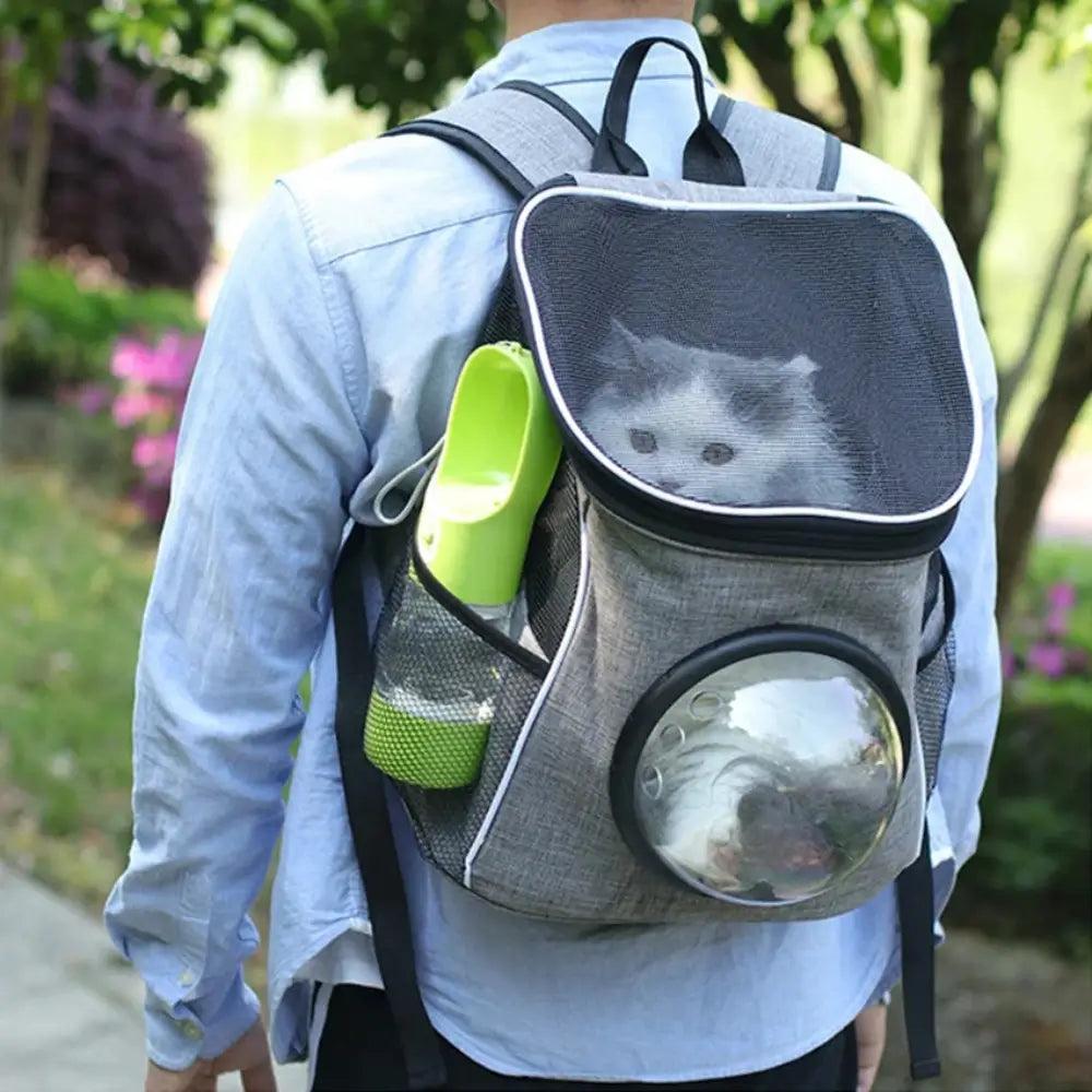 A man walking along outdoors carrying a pet travelling backpack containing a cat and a portable pet feeding bottle in green.